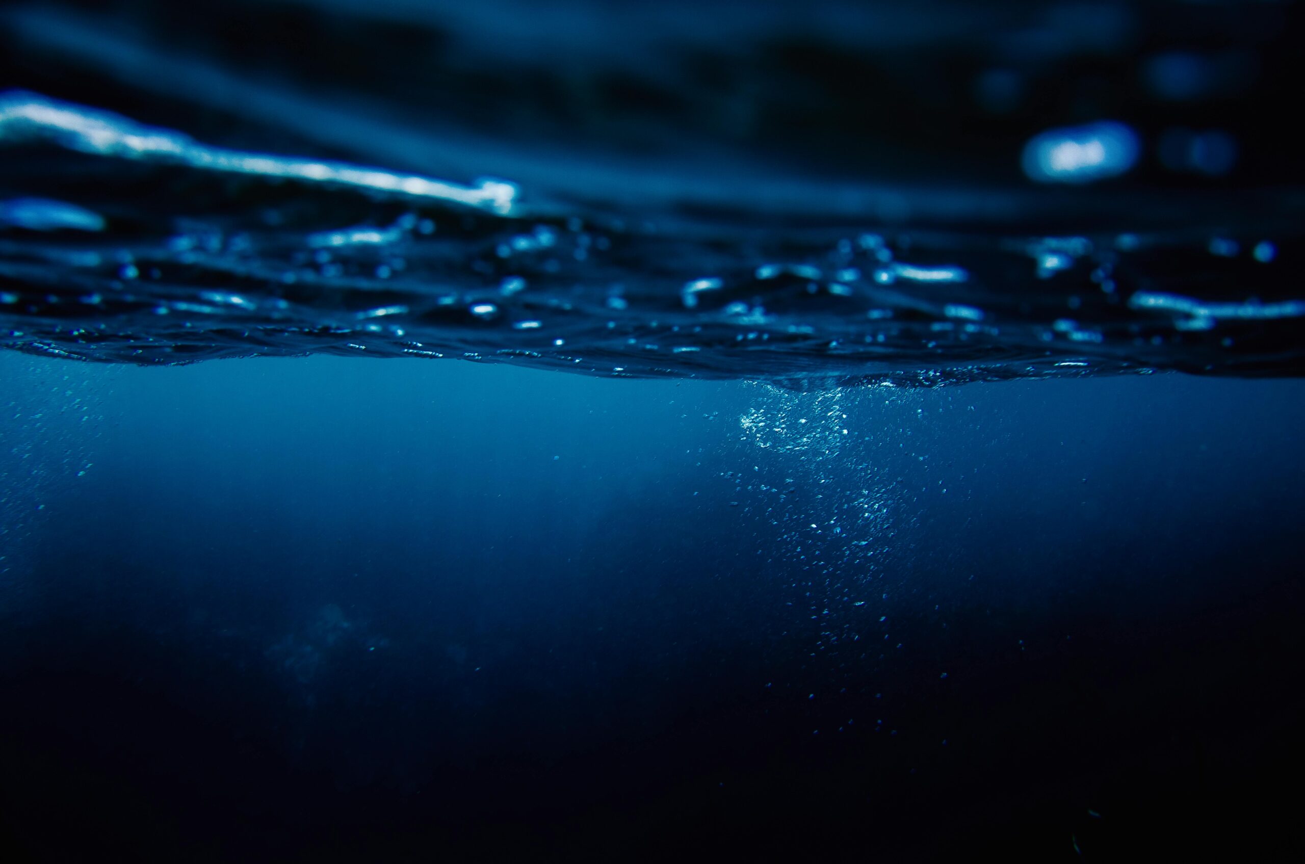A serene underwater scene capturing air bubbles rising to the ocean's surface at night.